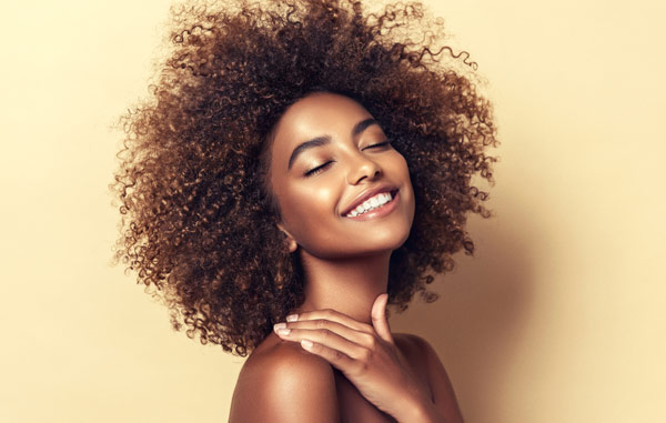 Smiling woman with gorgeous skin from pure radiance treatment and afro-textured hair on a pale yellow background from The Facial Center in Charleston, WV