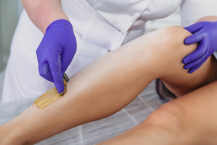 Beautician wearing purple latex gloves applies sugaring solution to a woman's leg at The Facial Center in Charleston, WV Beautician wearing purple latex gloves applies sugaring solution to a woman's leg at The Facial Center in Charleston, WV