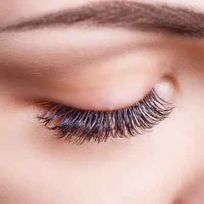 A hand holding neddle near cheeks of a woman with closed eyes