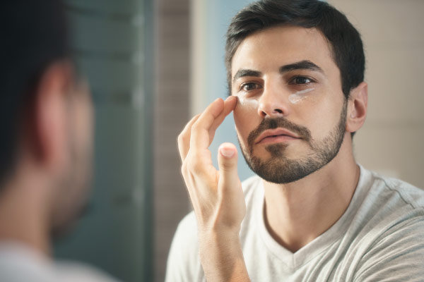 Handsome man using a mirror to apply Éminence skin care product to his face