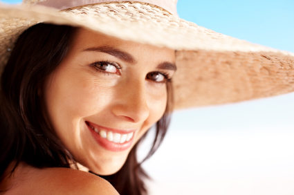Beautiful smiling woman wearing a hat to protect her glowing, flawless skin